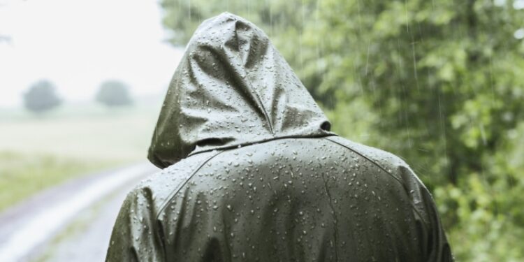 Rear view of woman in green raincoat walking in rain